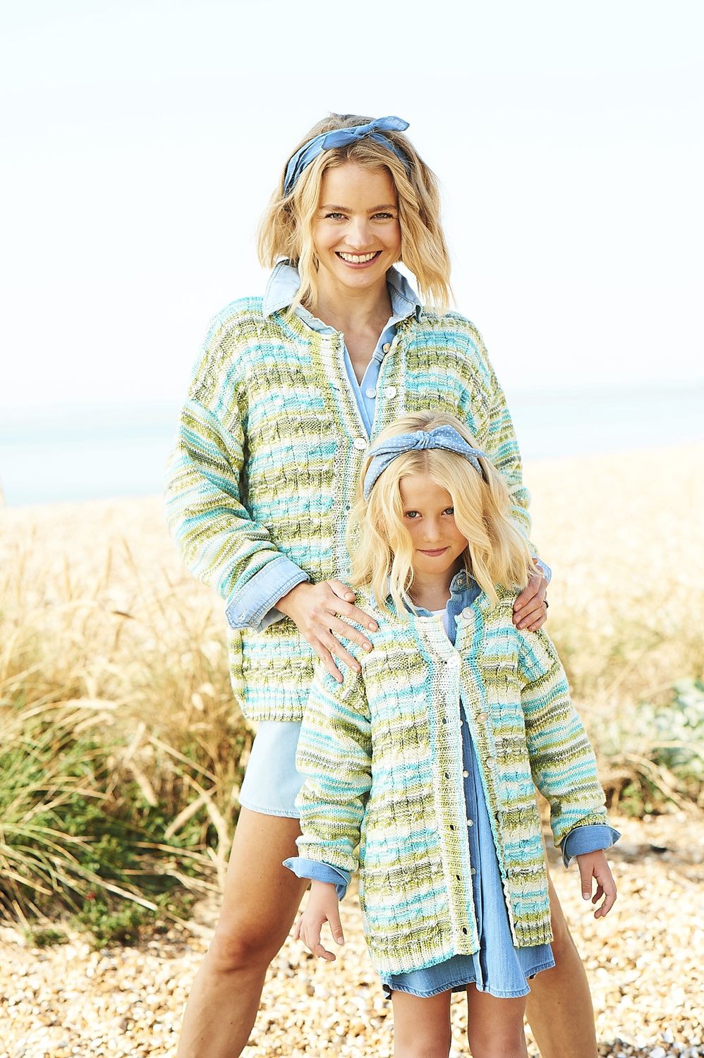 A woman and a girl are wearing matching knitted cardigans in a variegated blue and green yarn.
