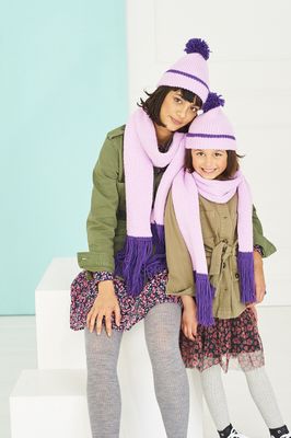 A woman and a girl are wearing matching pale purple and bright purple knitted hats and scarves.
