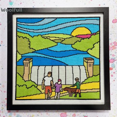 A framed cross stitch with a cartoon style design of Derwent Dam in the Peak District with people and a dog in front.