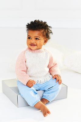 A baby is wearing a knitted sweater in cream and apricot.