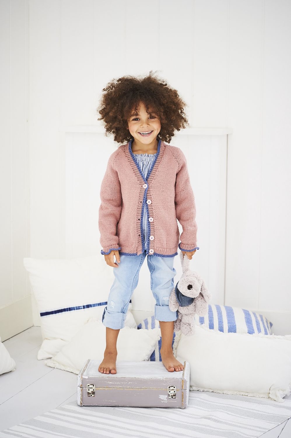 A girl is wearing a dusky pink knitted cardigan with blue trim.