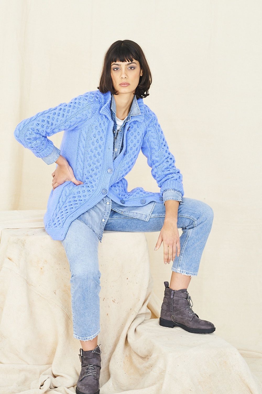 A woman is wearing a blue cable knit cardigan.