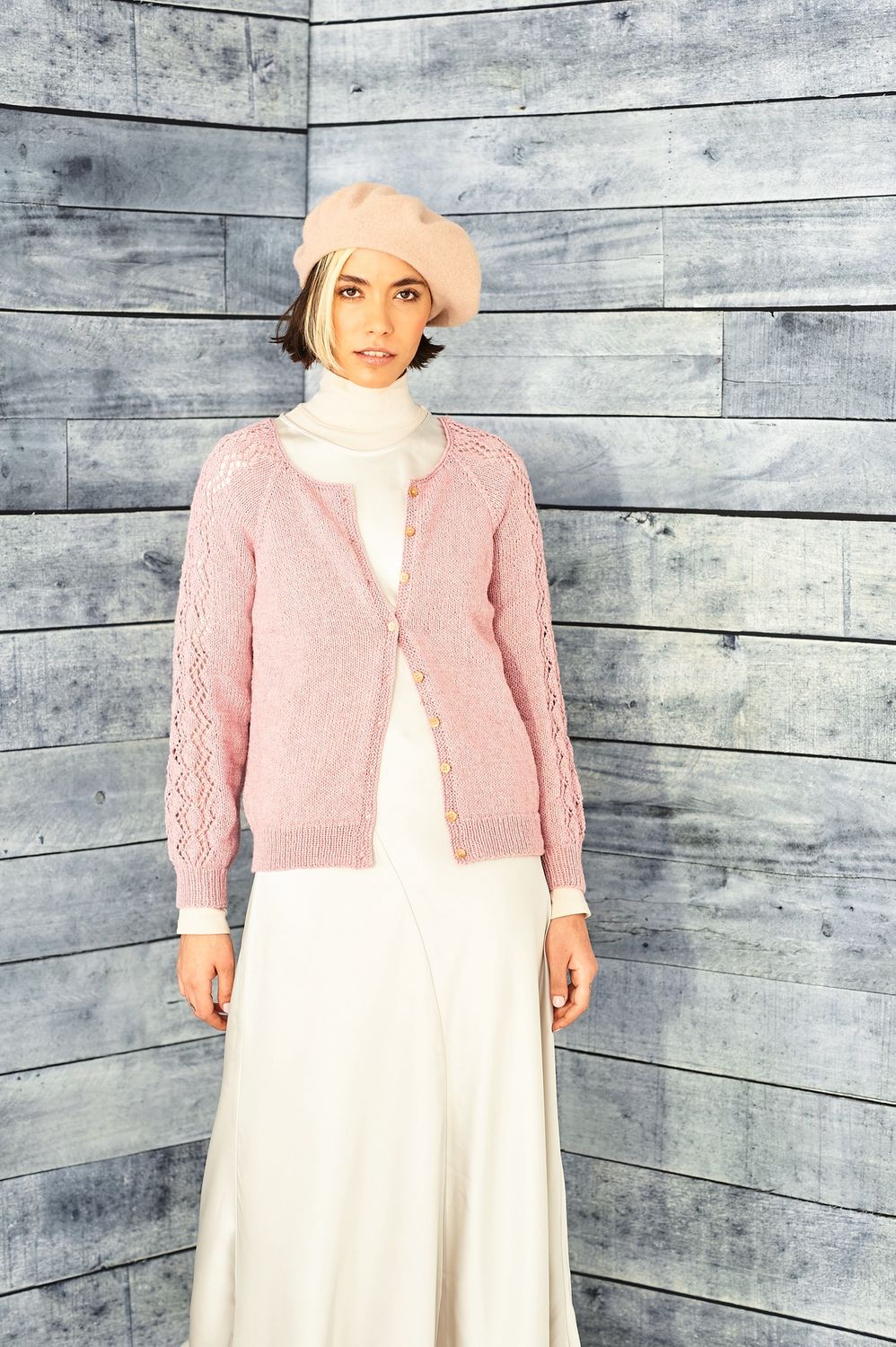 A woman is wearing a light pink knitted cardigan.