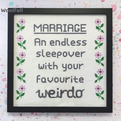 A framed cross stitch with a design that says &#39;marriage, an endless sleepover with your favourite weirdo&#39; in grey and purple and green flowers down each side.