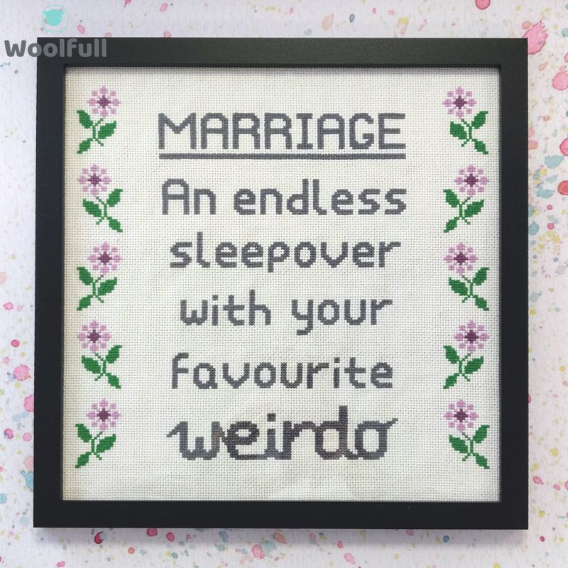 A framed cross stitch with a design that says &#39;marriage, an endless sleepover with your favourite weirdo&#39; in grey and purple and green flowers down each side.
