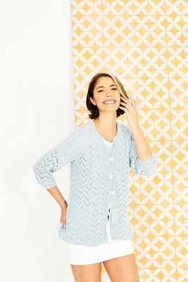 A woman is wearing a duck egg blue knitted cardigan with zig zag lace detail.