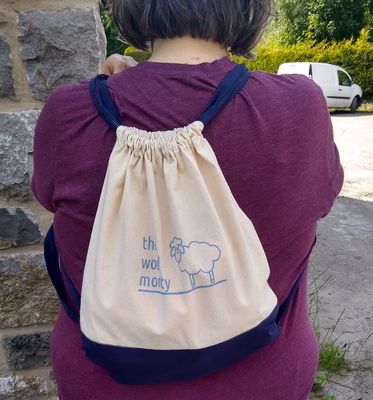 A cream drawstring bag with navy blue base and straps and &#39;The Wool Monty&#39; logo in the centre.