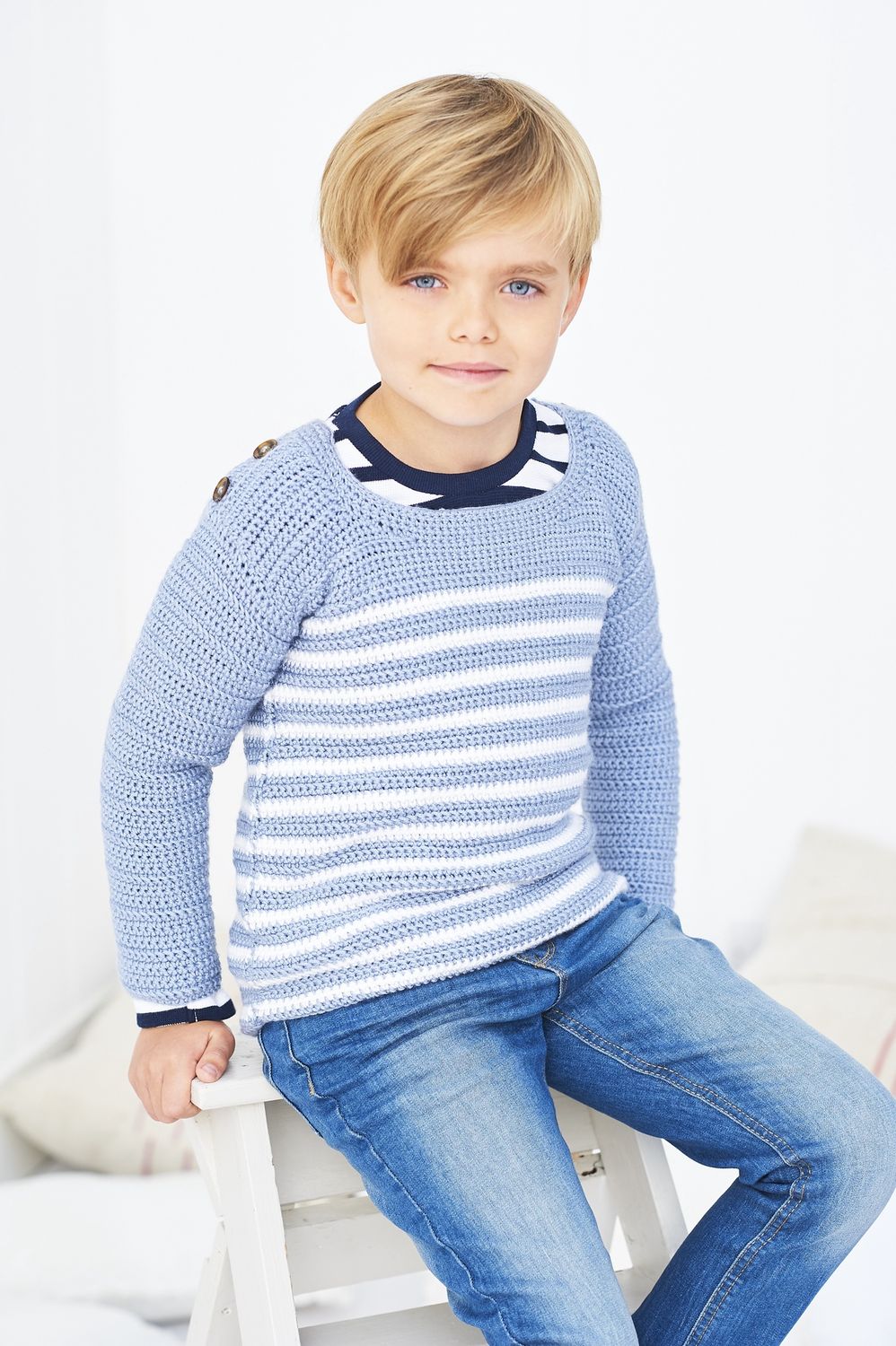 A child is wearing a blue crocheted sweater with white stripes.