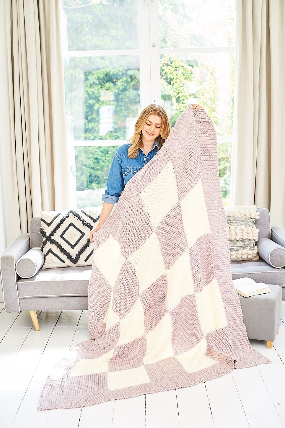 A woman is holding a knitted blanket made of pink and cream squares.