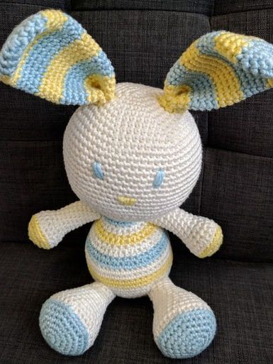 A crocheted toy rabbit in cream, blue and yellow.