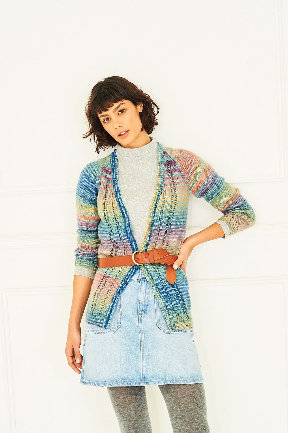 A woman is wearing a knitted cardigan in shades of blue, red, orange, yellow, green and purple.
