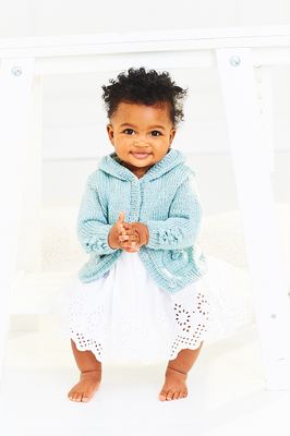 A baby is wearing a blue knitted hooded cardigan with flower detail on the sleeves and pockets.