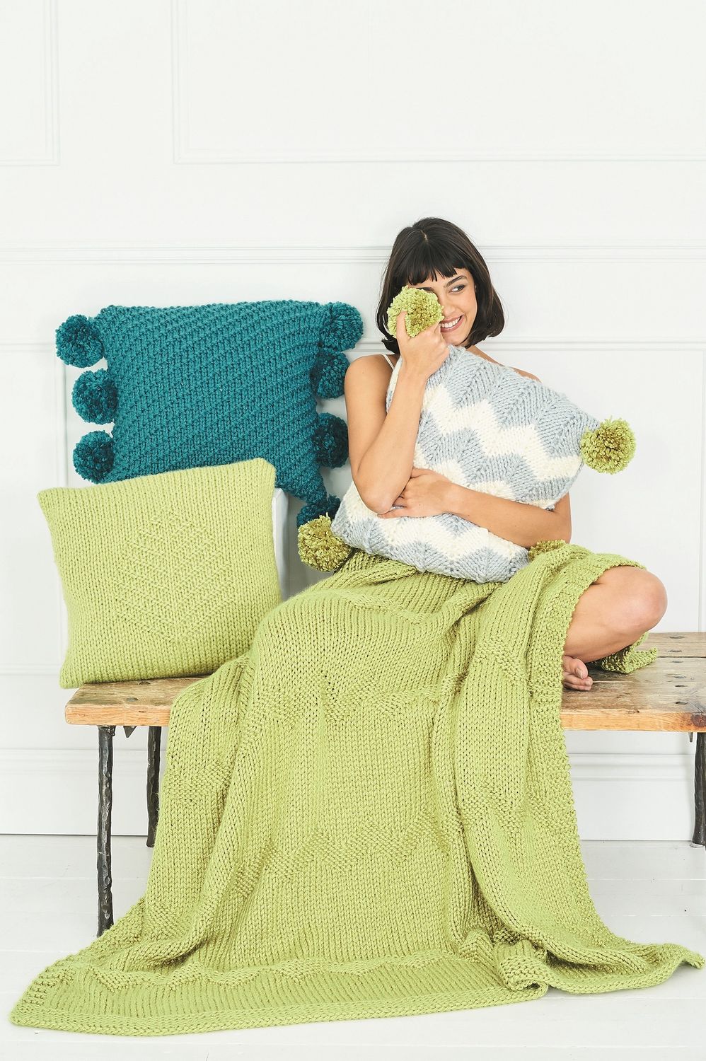 A pale green knitted blanket along with 3 knitted cushions.