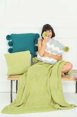 A pale green knitted blanket along with 3 knitted cushions.