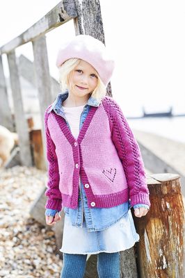 A girl is wearing a light pink knitted cardigan with dark pink sleeves and lace heart detail.