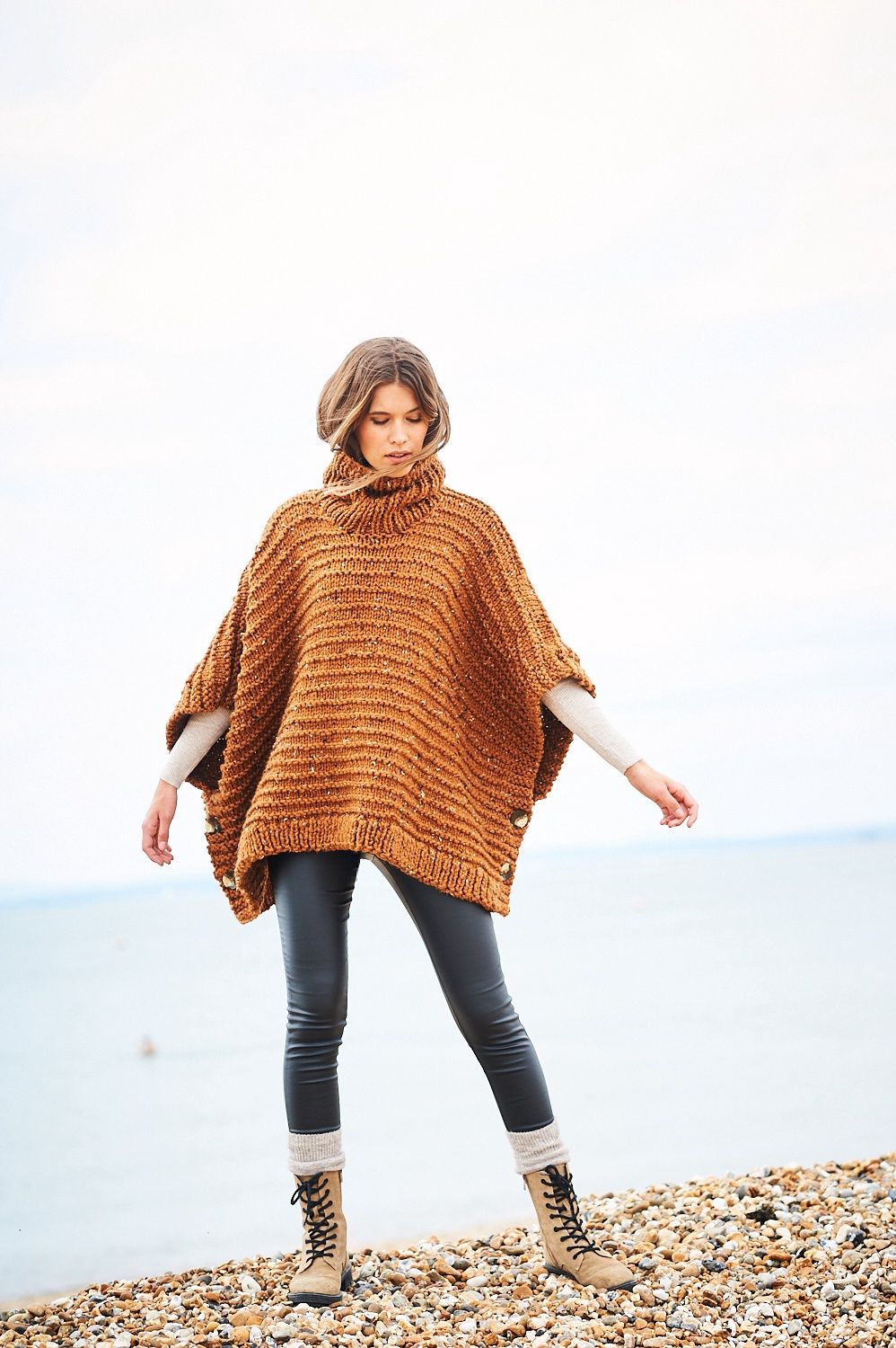 A woman is wearing an orange-brown knitted textured poncho.