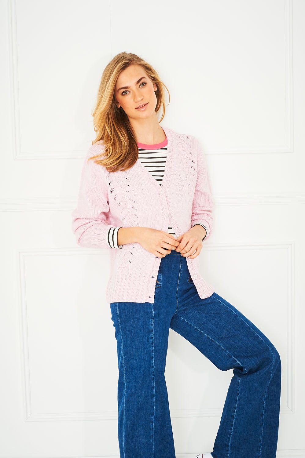 A woman is wearing a pale pink knitted cardigan.