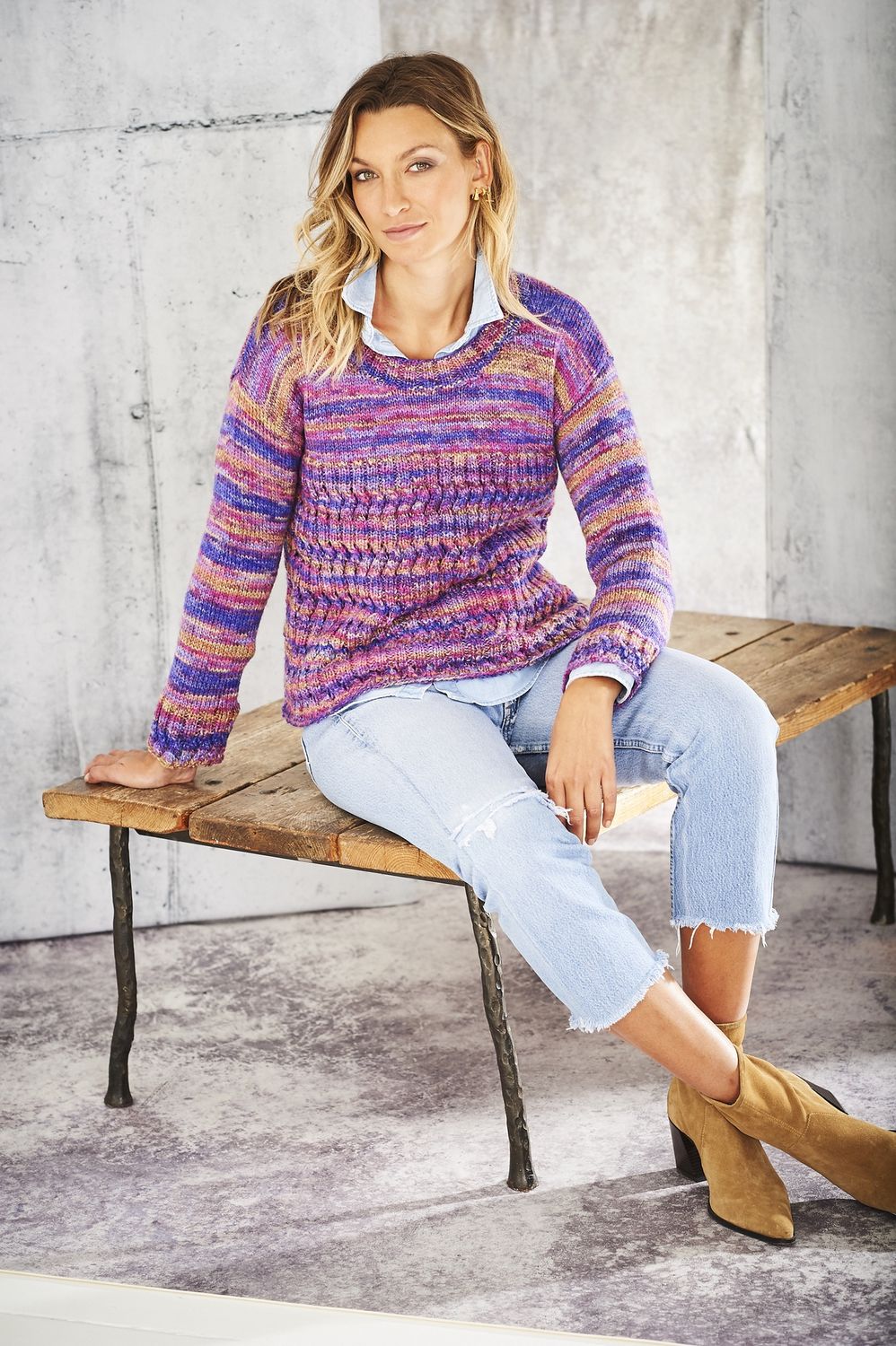 A woman is wearing a knitted sweater in a variegated purple yarn.