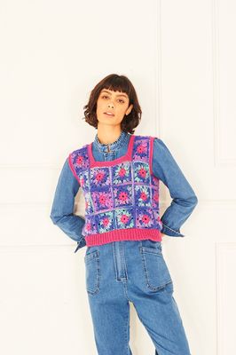 A woman is wearing a crocheted sweater in shades of blue, pink, and purple.