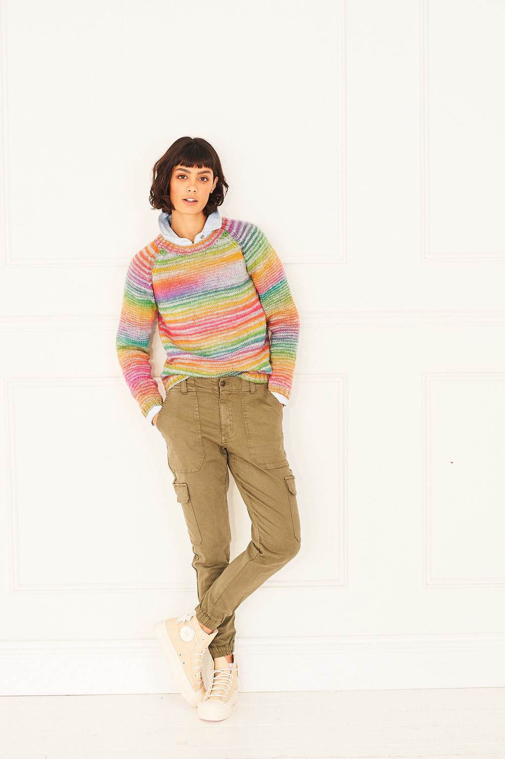 A woman is wearing a knitted sweater in shades of grey, red, orange, yellow, green and purple.