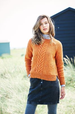 A woman is wearing an orange knitted sweater with cable down the front centre.
