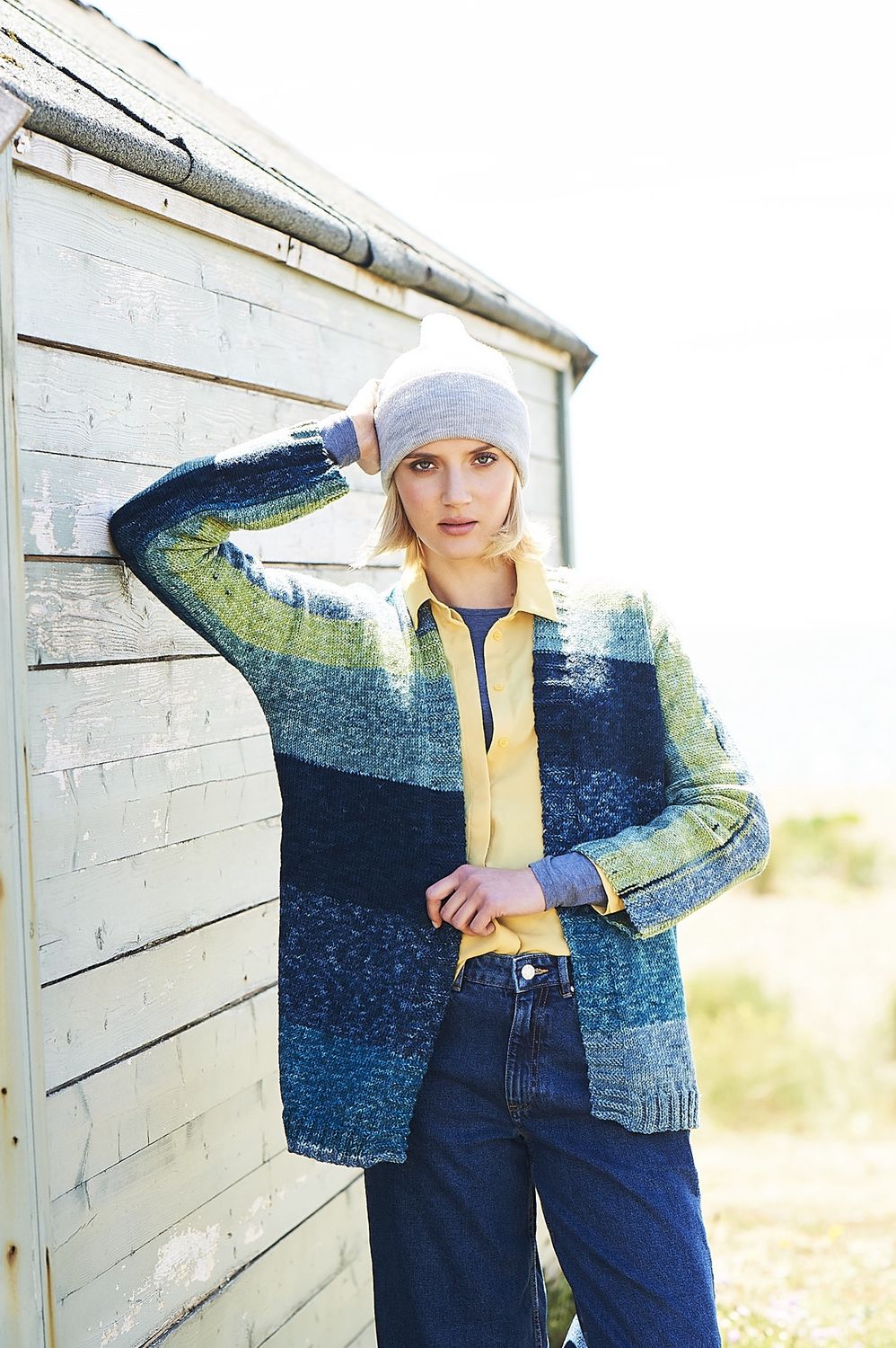 A woman is wearing a knitted cardigan in blue and green stripes.