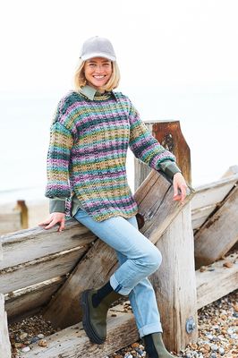 A woman is wearing a variegated knitted sweater in shades of blue, green, purple and teal.