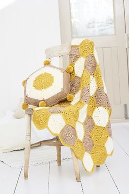 A crocheted blanket made up of yellow, cream and light brown hexagons, along with a matching cushion.