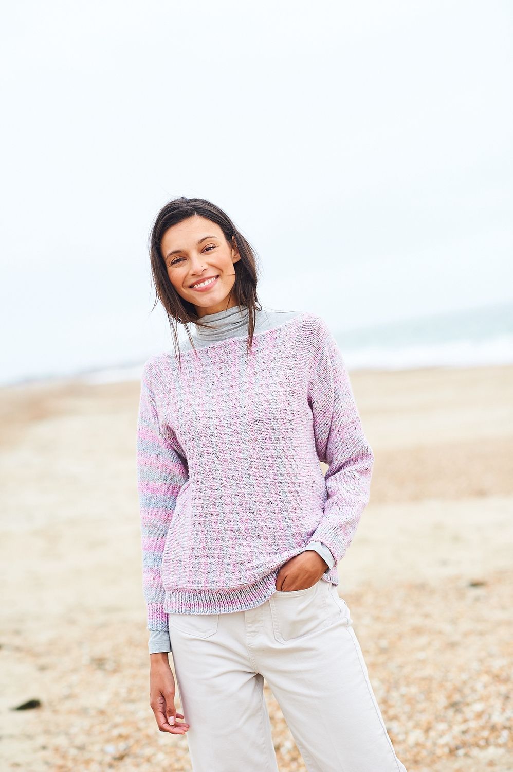 A woman is wearing a knitted sweater in shades of pink and blue.