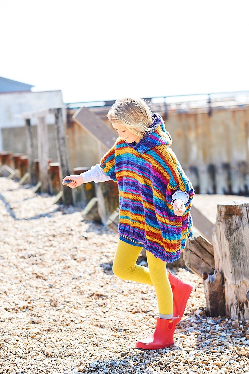 A girl is wearing a variegated knitted poncho in shades of blue, yellow, red and purple.