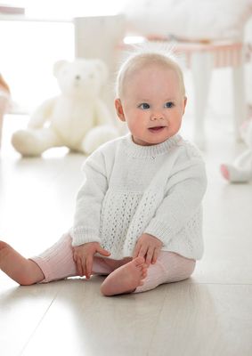 A baby is wearing a white knitted sweater.