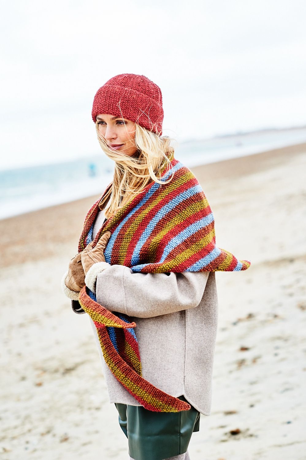 A woman is wearing a red knitted hat and a red, blue, brown and green striped knitted shawl.