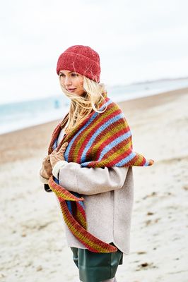 A woman is wearing a red knitted hat and a red, blue, brown and green striped knitted shawl.