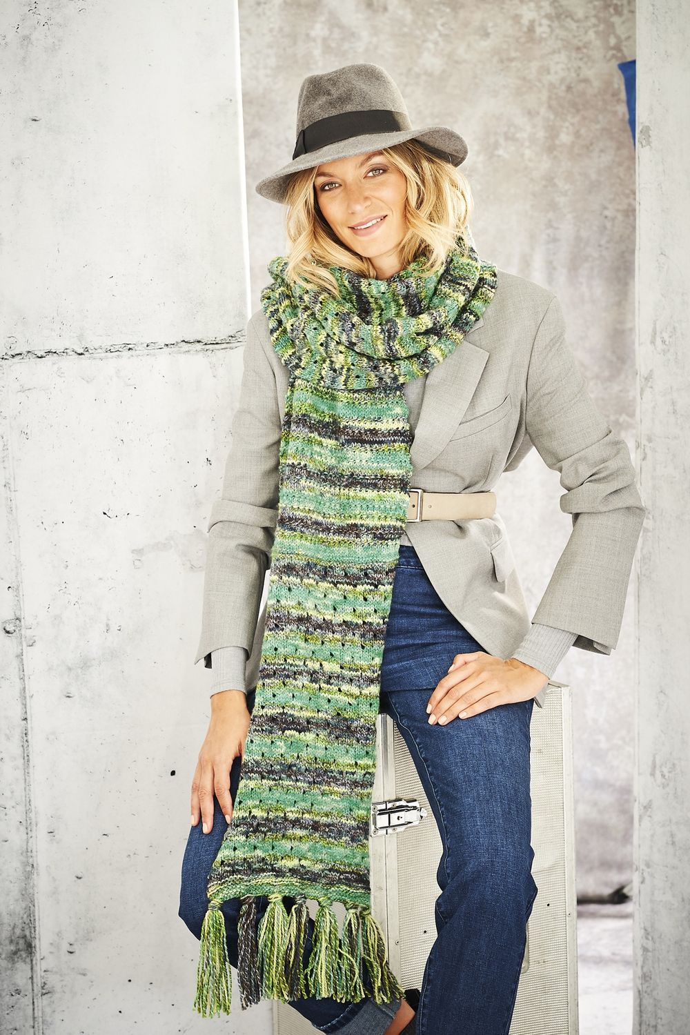 A woman is wearing a knitted scarf in a variegated green yarn.