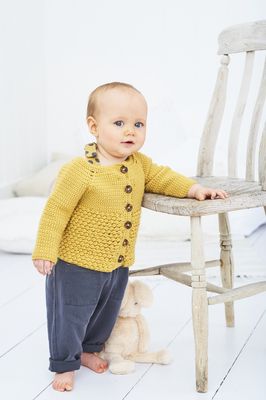 A baby is wearing a yellow crocheted cardigan.