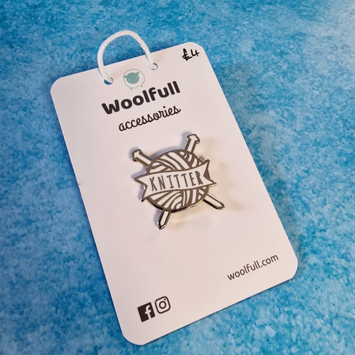 A blue background with a silver and white ball of yarn shaped pin badge with the word &#39;knitter&#39; in the centre.
