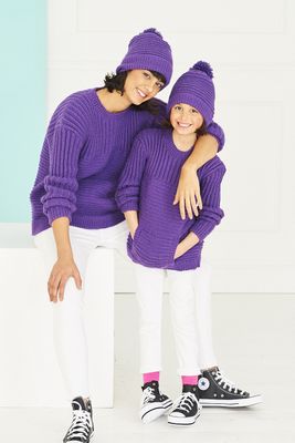 A woman and a girl are both wearing purple knitted sweaters and purple knitted hats.