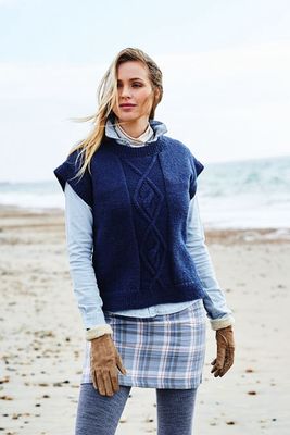 A woman on the beach is wearing a dark blue slipover with cable detail on the front.