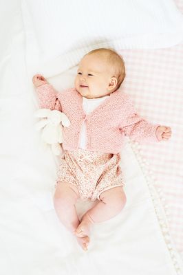 A baby is wearing a pink knitted cardigan.