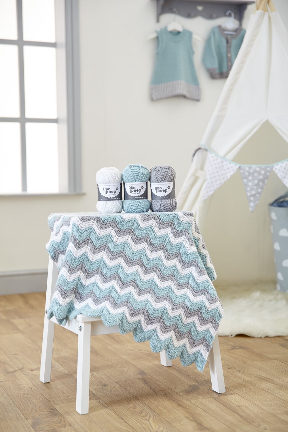 A zig zag knitted baby blanket in cream, grey and pale blue.