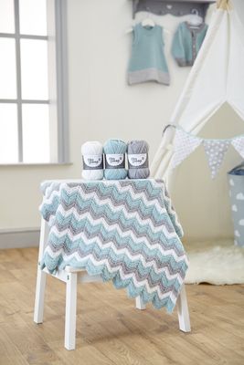 A zig zag knitted baby blanket in cream, grey and pale blue.
