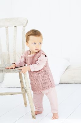 A baby is wearing a dusky pink crocheted dress.