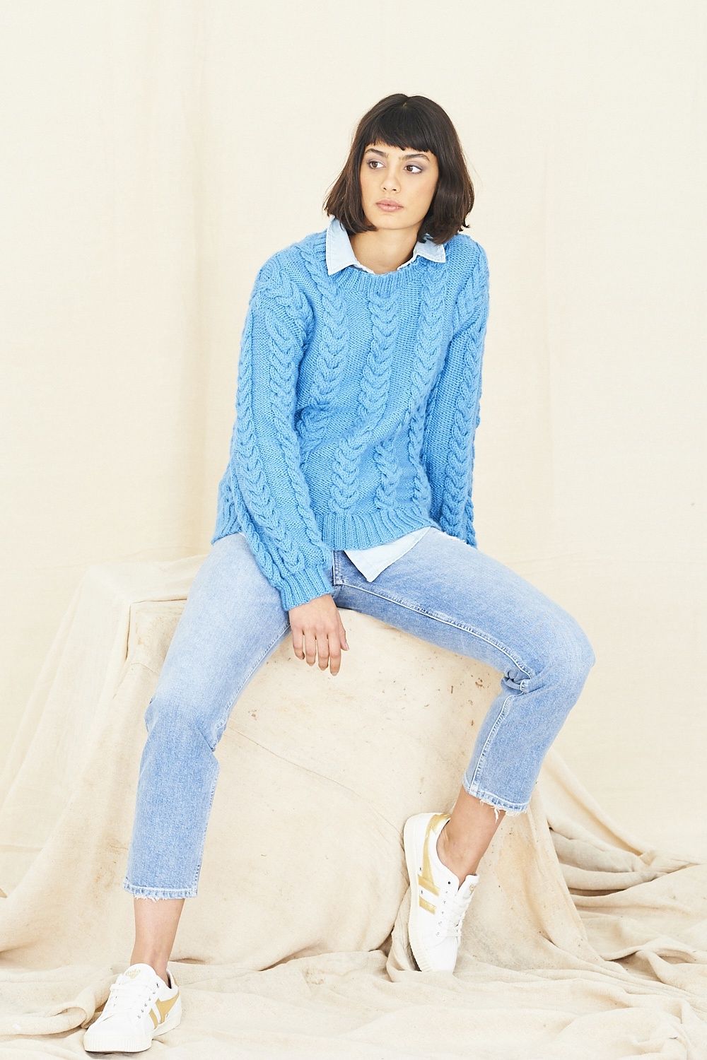 A woman is wearing a blue cable knit sweater.