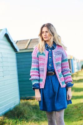 A woman is wearing a knitted cardigan in shades of pink, purple and teal.
