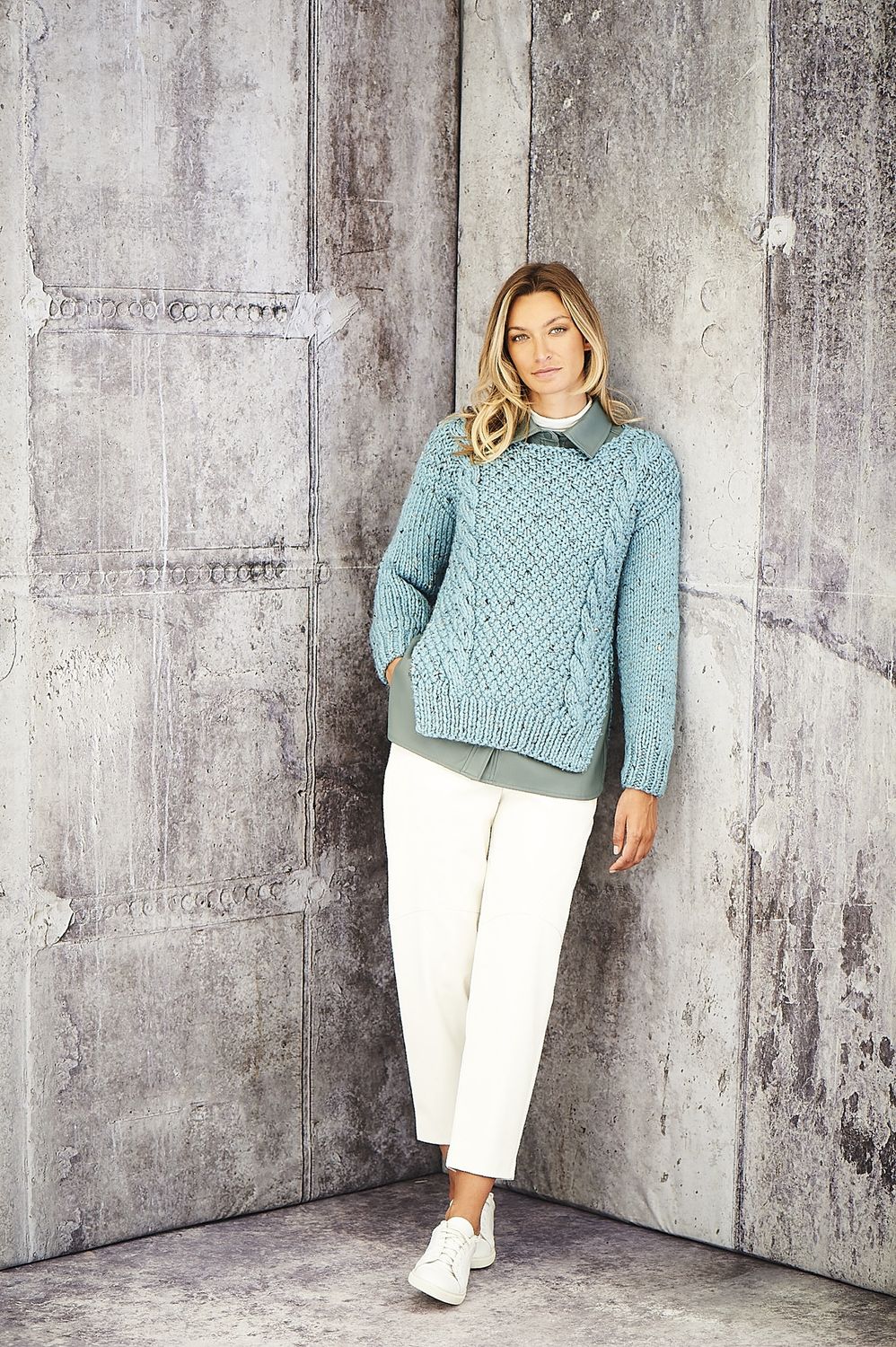 A woman is wearing a blue cable knit sweater.