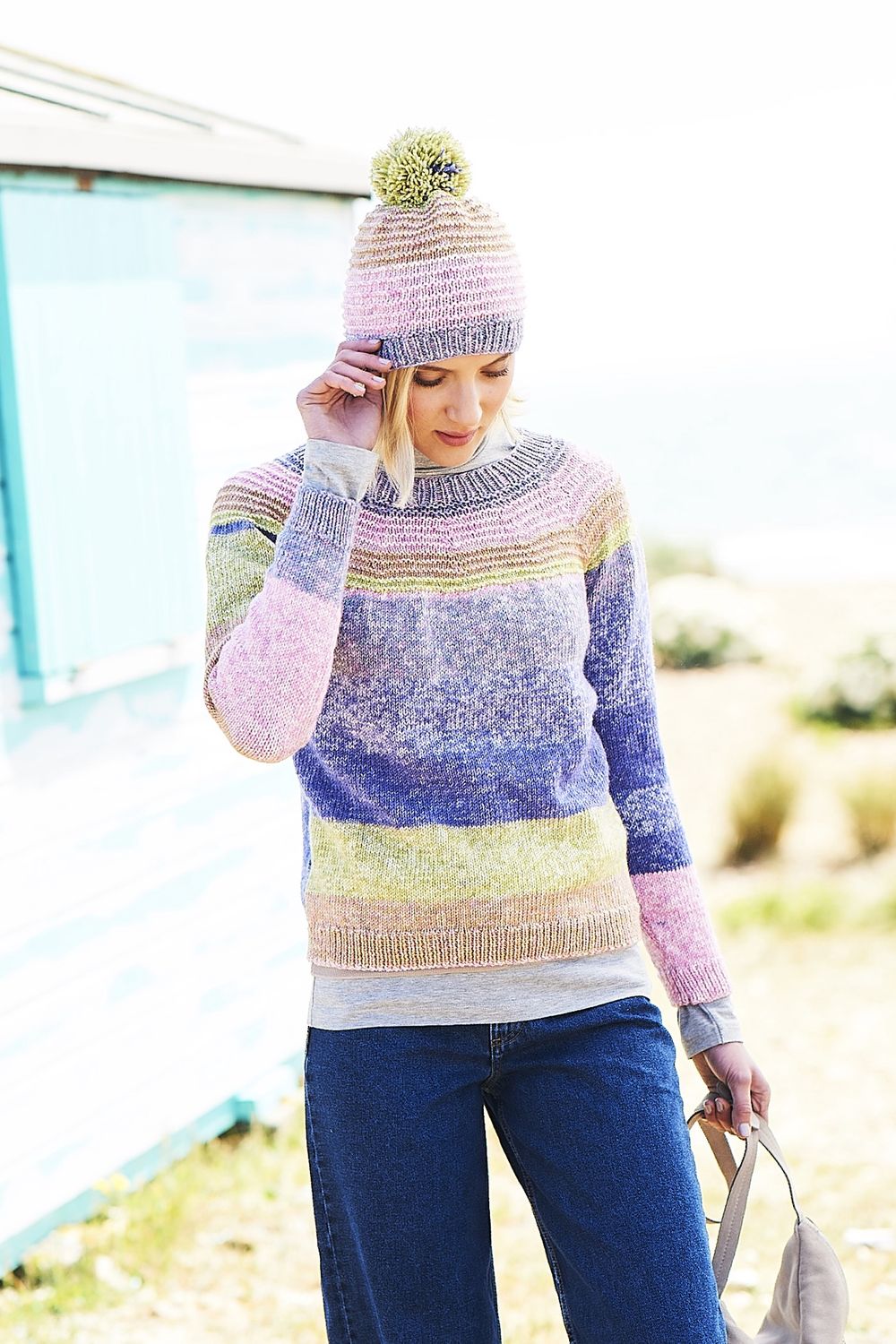 A woman is wearing a knitted sweater and matching hat in purple, green, pink and brown stripes.