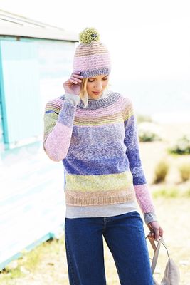A woman is wearing a knitted sweater and matching hat in purple, green, pink and brown stripes.