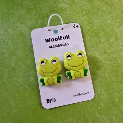 A green background with a pair of frog shaped point protectors mounted on a white card.