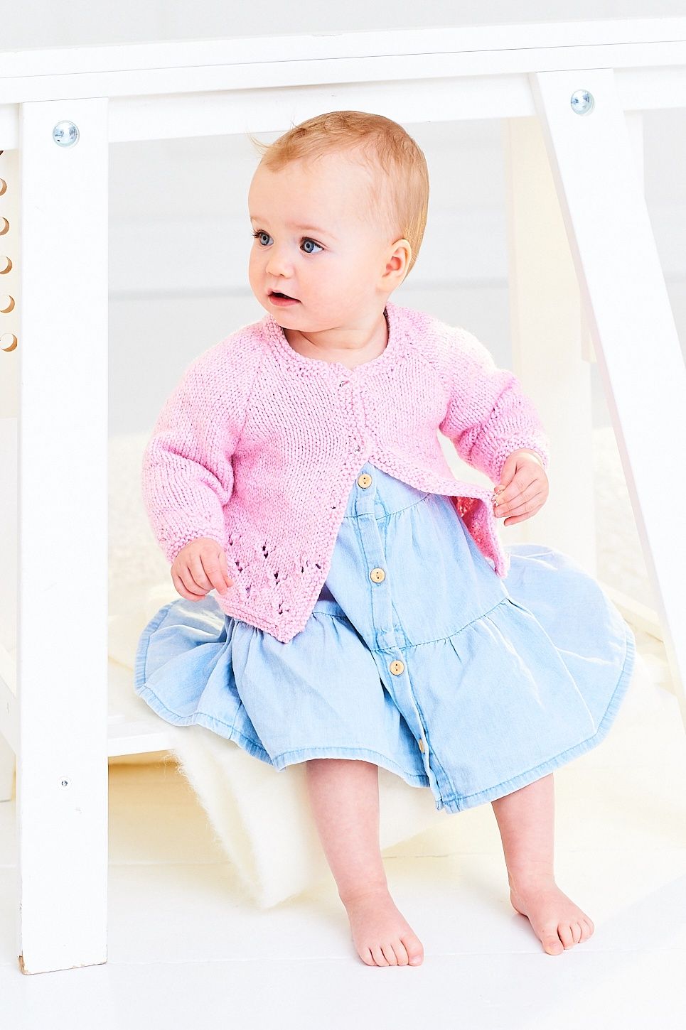 A baby is wearing a knitted pink cardigan.