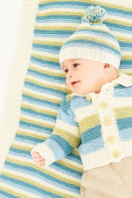 A close up of a baby wearing a knitted cardigan and matching hat in blue, green and cream stripes, while laying on a matching blanket.
